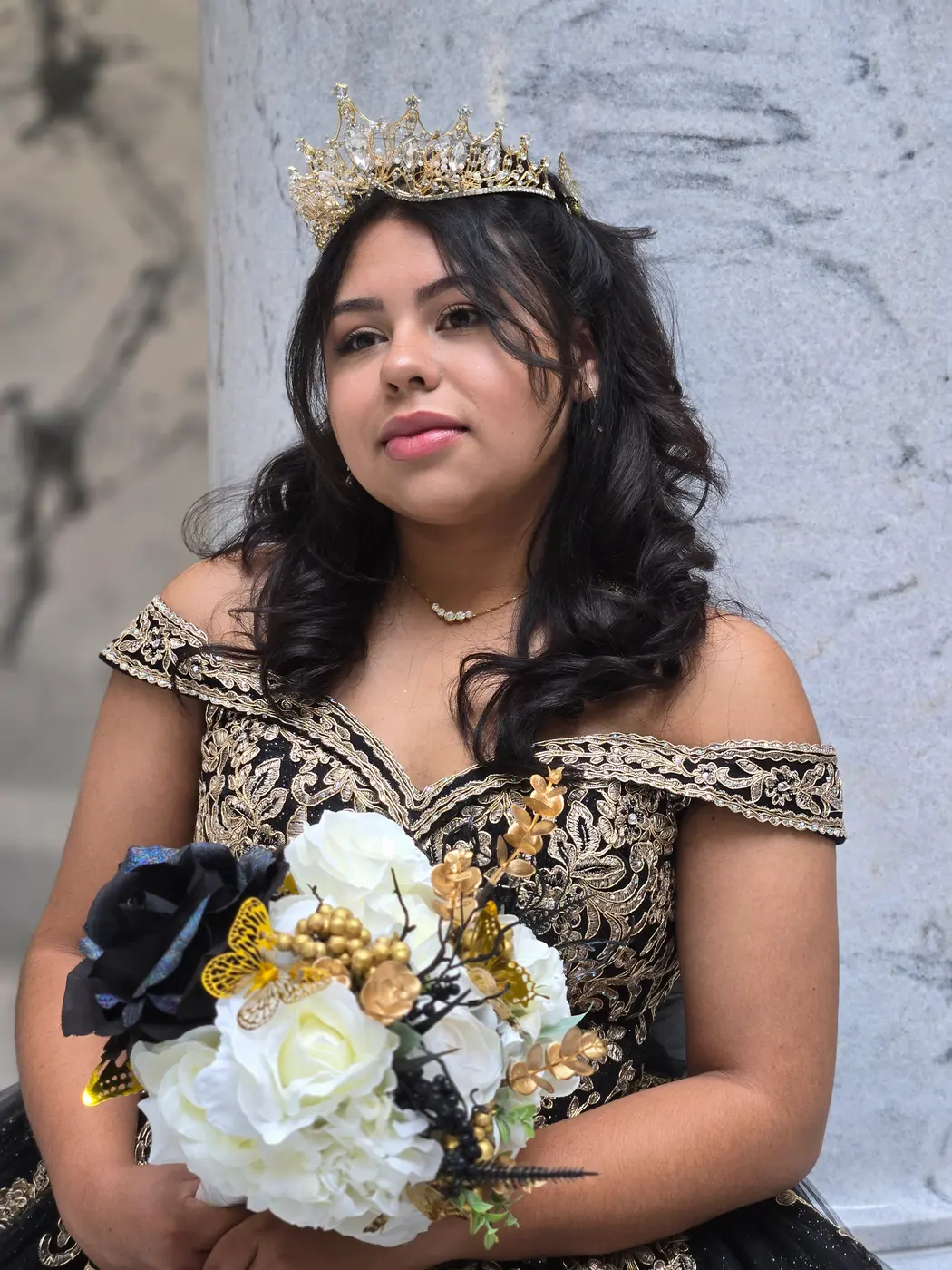 Quinceañera con corona y vestido negro con dorado sosteniendo su ramo