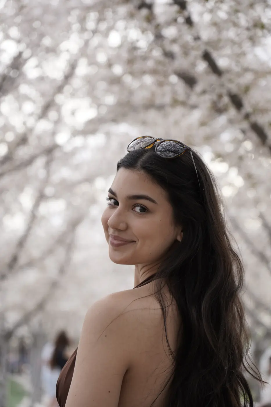 Joven sonriendo por encima del hombro entre cerezos en flor