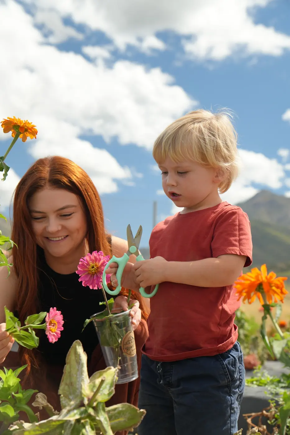 Mamá sonríe mientras su hijo corta flores con unas tijeras en un campo de zinnias